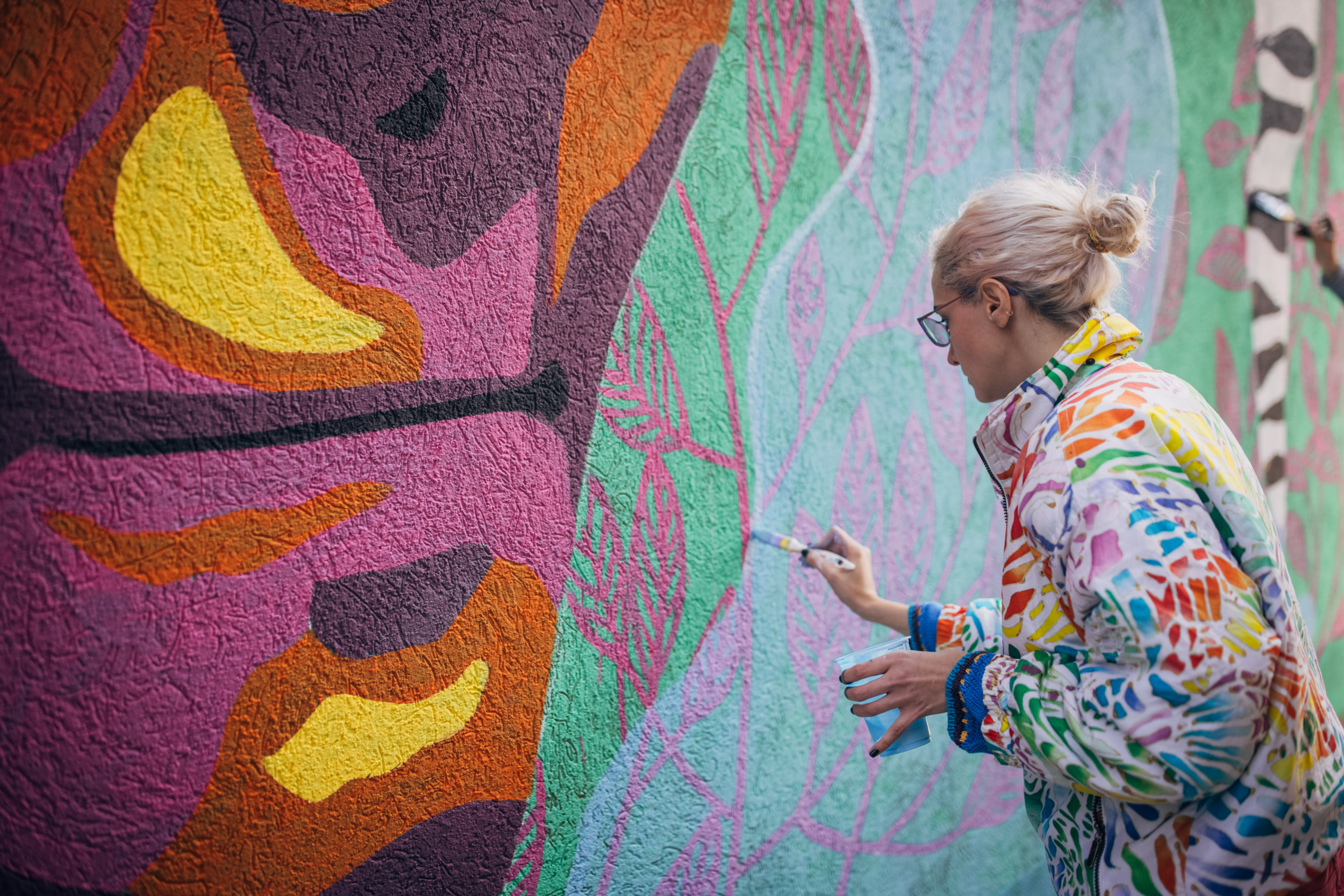 Female artist painting on wall during PANELS'22